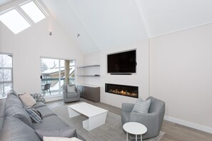 Relax in this stylish living room with a grey sofa, armchair, and flat-screen TV, complemented by a fireplace and large window.