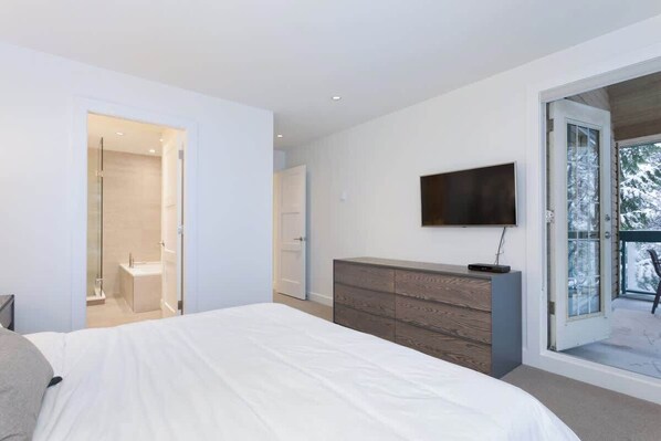 Een slaapkamer met een groot bed, een dressoir, een aan de muur bevestigde televisie en een schuifdeur naar een balkon.