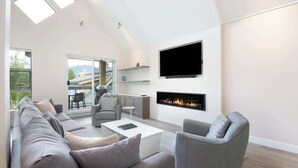 A modern living room with a fireplace, a flat-screen TV, and a large window overlooking a balcony.