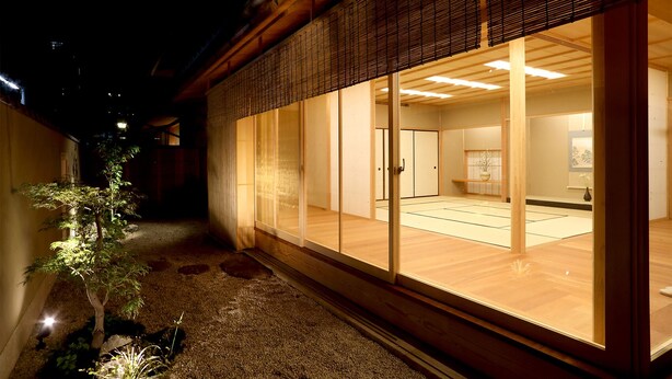 A traditional Japanese building with tatami mat flooring, sliding doors, and a small garden area with a tree. - Maru Izumiyacho (Kyoto)