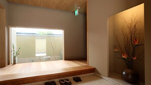 A room with a wooden bench, a vase with flowers, and a view through a glass door. - Maru Izumiyacho (Kyoto)