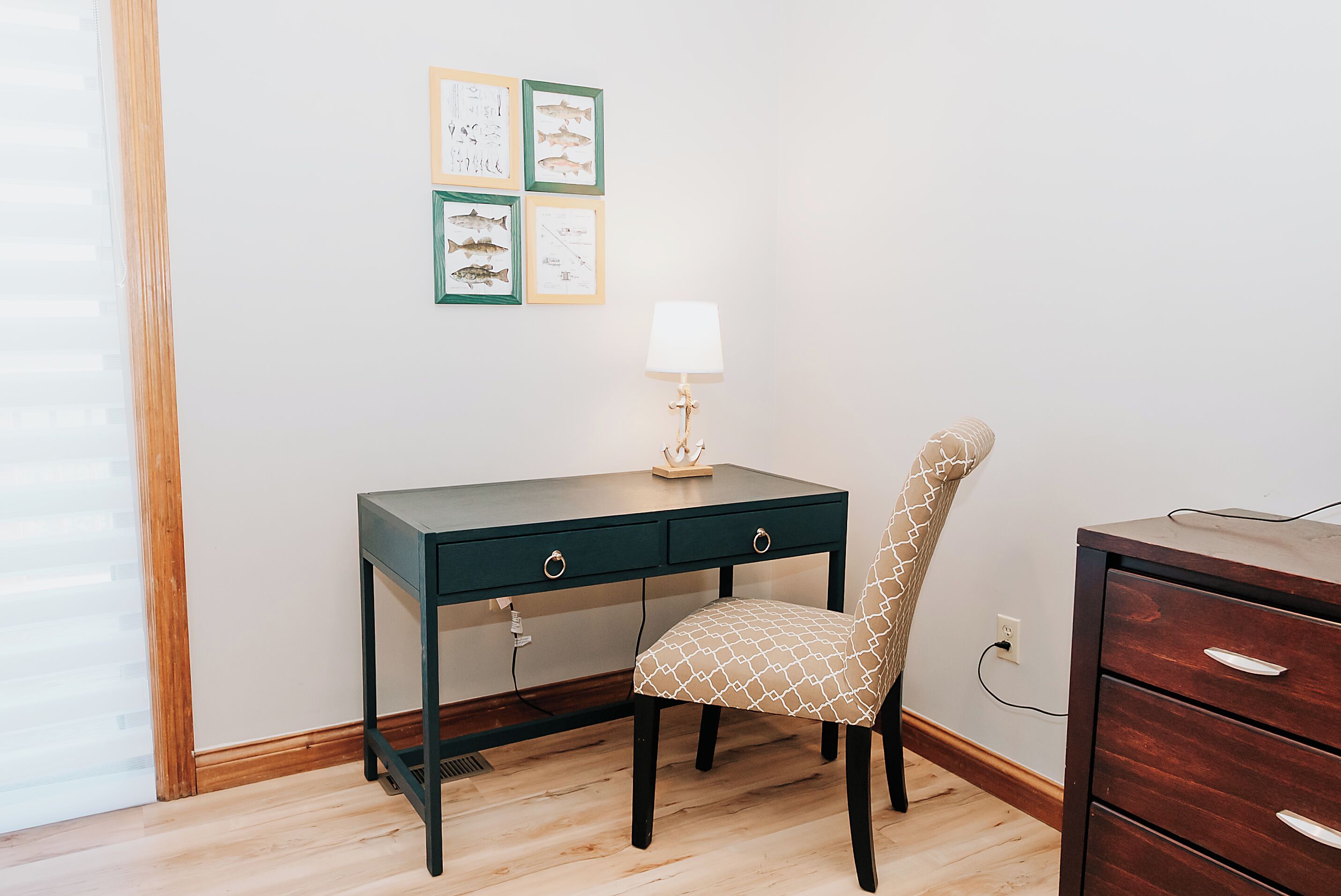 Une pièce comprenant un bureau, une chaise, une lampe et des illustrations de poissons encadrées accrochées au mur.