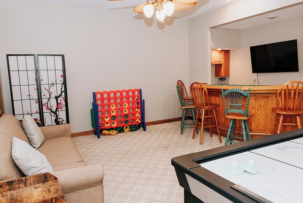 A living room with a sofa, a coffee table, a TV, and a bar area with chairs.