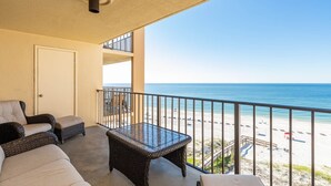 Un balcon agrémenté de meubles en osier, d’une table en verre et offrant une vue sur la plage.