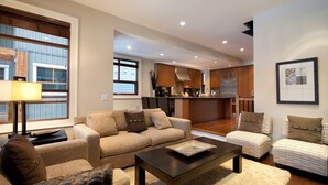Un salon moderne avec un canapé, des fauteuils, une table basse et une cuisine en arrière-plan.