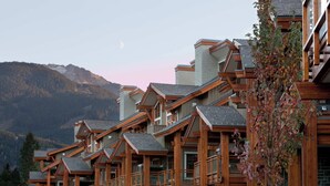 Un chalet en bois à plusieurs étages, doté de balcons, qui se dresse sur un fond de paysage montagneux.