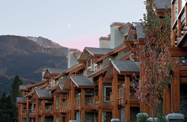 A multi-story wooden building with balconies, set against a mountainous backdrop.