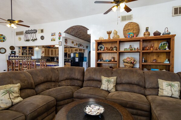 A living room with a sectional sofa, a coffee table, and a kitchen in the background.