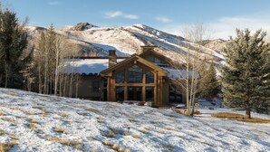 A wooden cabin with large windows, surrounded by snow-covered ground and trees, with mountains in the background. - 2 Miles to Downtown Ketchum | Game Room (Sun Valley)
