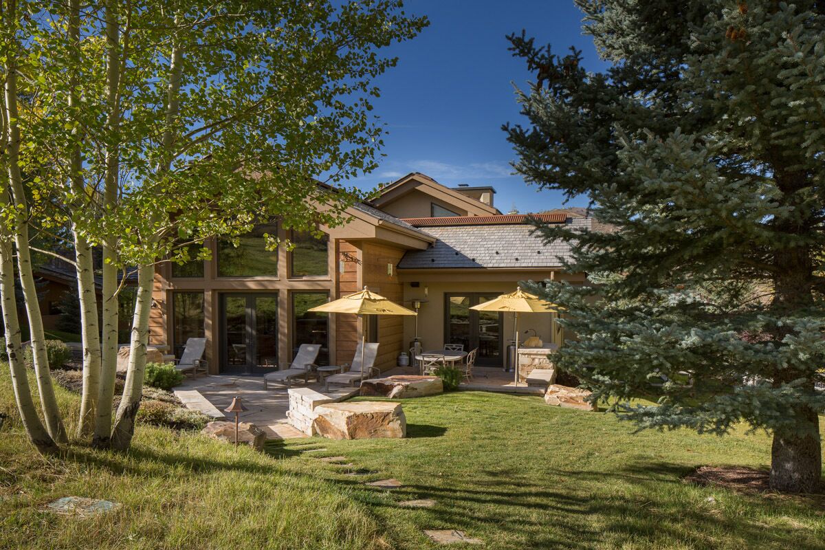 A modern house with a patio area, outdoor seating, and a large tree in the foreground.