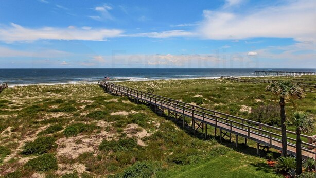 Ein Küstenwanderweg mit Holzdeck, der zu einem Strandabschnitt mit Dünen und Meerblick führt.