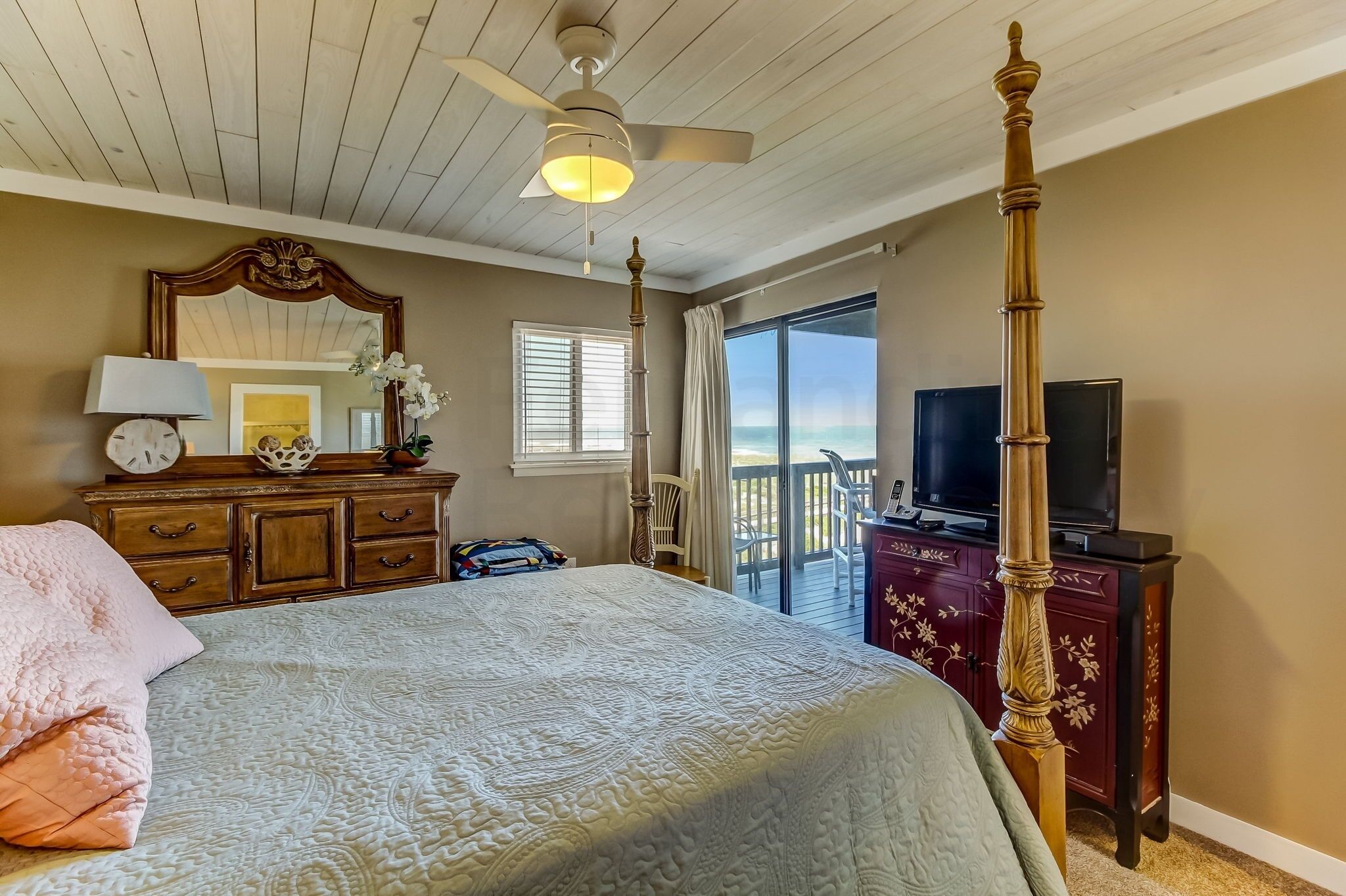 Quarto com cama grande, ventilador de teto, televisão e varanda com vista.