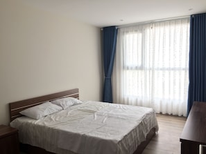 A bedroom with a single bed, a wooden headboard, a nightstand, and a window with sheer curtains and a blue drape. - Northern Stella Homestay (Hanoi)