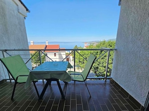 Un balcón con una mesa y dos sillas, con vistas a un paisaje que incluye agua y edificios.