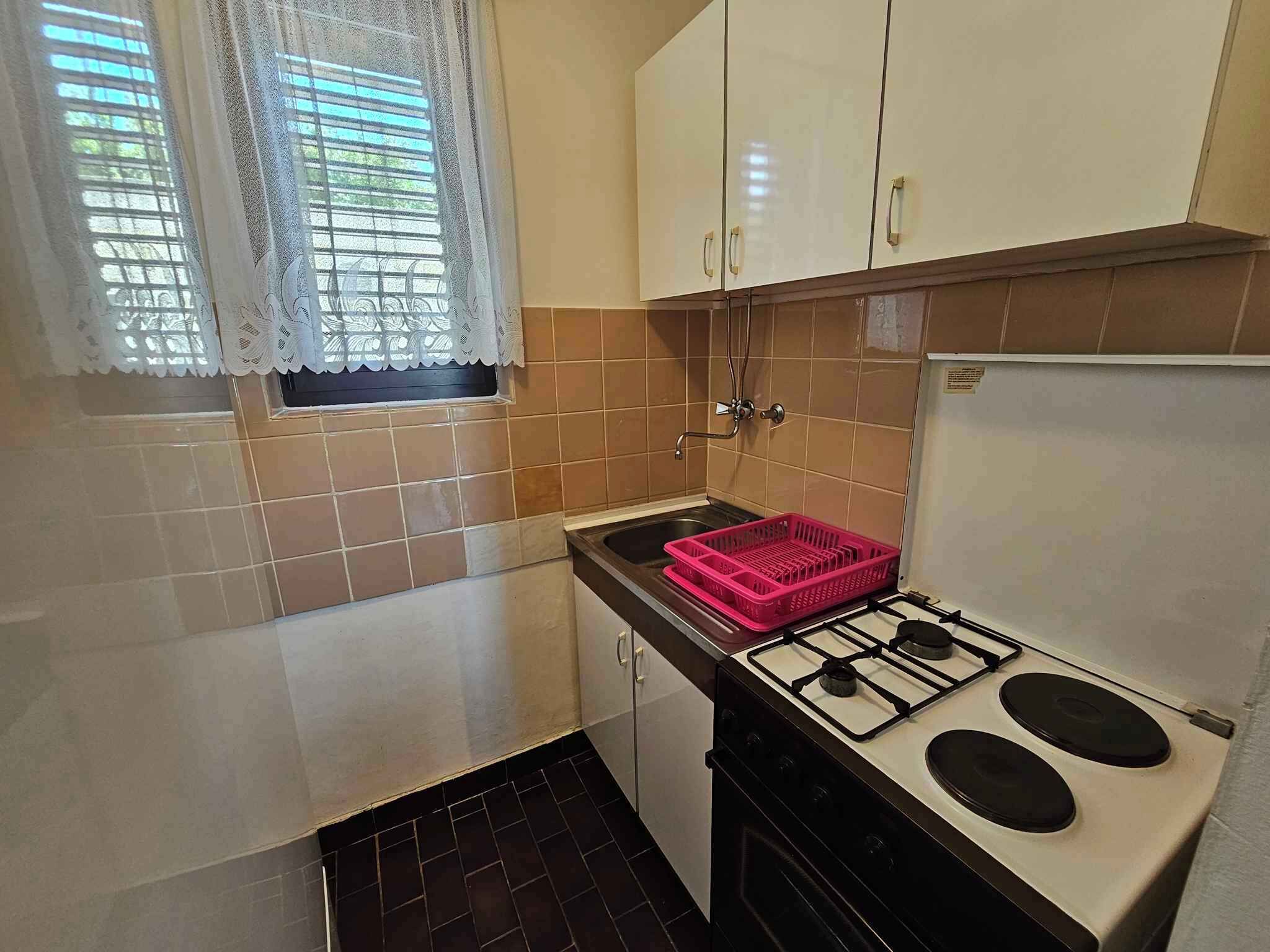 A compact kitchen with a gas stove, a sink, and a window with lace curtains.