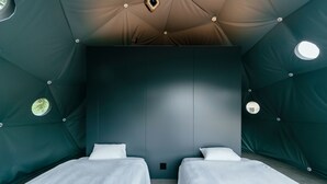 Una habitación con dos camas, techo oscuro y lámparas circulares.