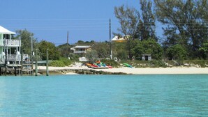 A coastal property with a house on stilts, a dock, and kayaks on the beach. - Cozy Cottage Perfect for 2 (Exuma)