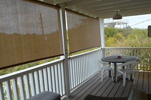 A covered outdoor area with a white railing, a table with chairs, and a view of greenery and a building in the background. - Cozy Cottage Perfect for 2 (Exuma)