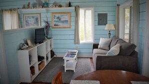 A cozy living room with a blue wall, a grey sofa, a wooden coffee table, and a television on a white stand. - Cozy Cottage Perfect for 2 (Exuma)