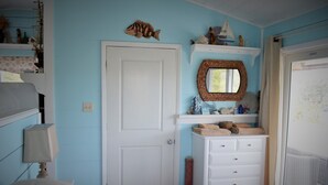 A bedroom with a bed, a dresser, a mirror, and shelves with decorative items. - Cozy Cottage Perfect for 2 (Exuma)