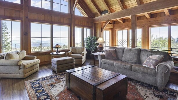 A spacious living room with large windows, wooden beams, and a cozy seating area. - Glacier Luxury Lodge 360 Views (Truckee)