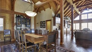 A spacious dining area with a wooden table and chairs, a large rug, and a high ceiling with exposed beams. - Glacier Luxury Lodge 360 Views (Truckee)