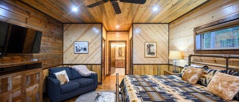 Een slaapkamer in een blokhut met een bed, een bank, een televisie en een plafondventilator.