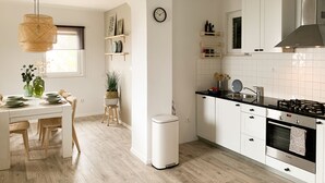 Una cocina moderna con armarios blancos, una estufa de acero inoxidable y un comedor con mesa y sillas blancas.