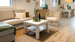 Una sala de estar moderna con un sofá, una silla de mimbre, una mesa de comedor con sillas y una lámpara colgante.