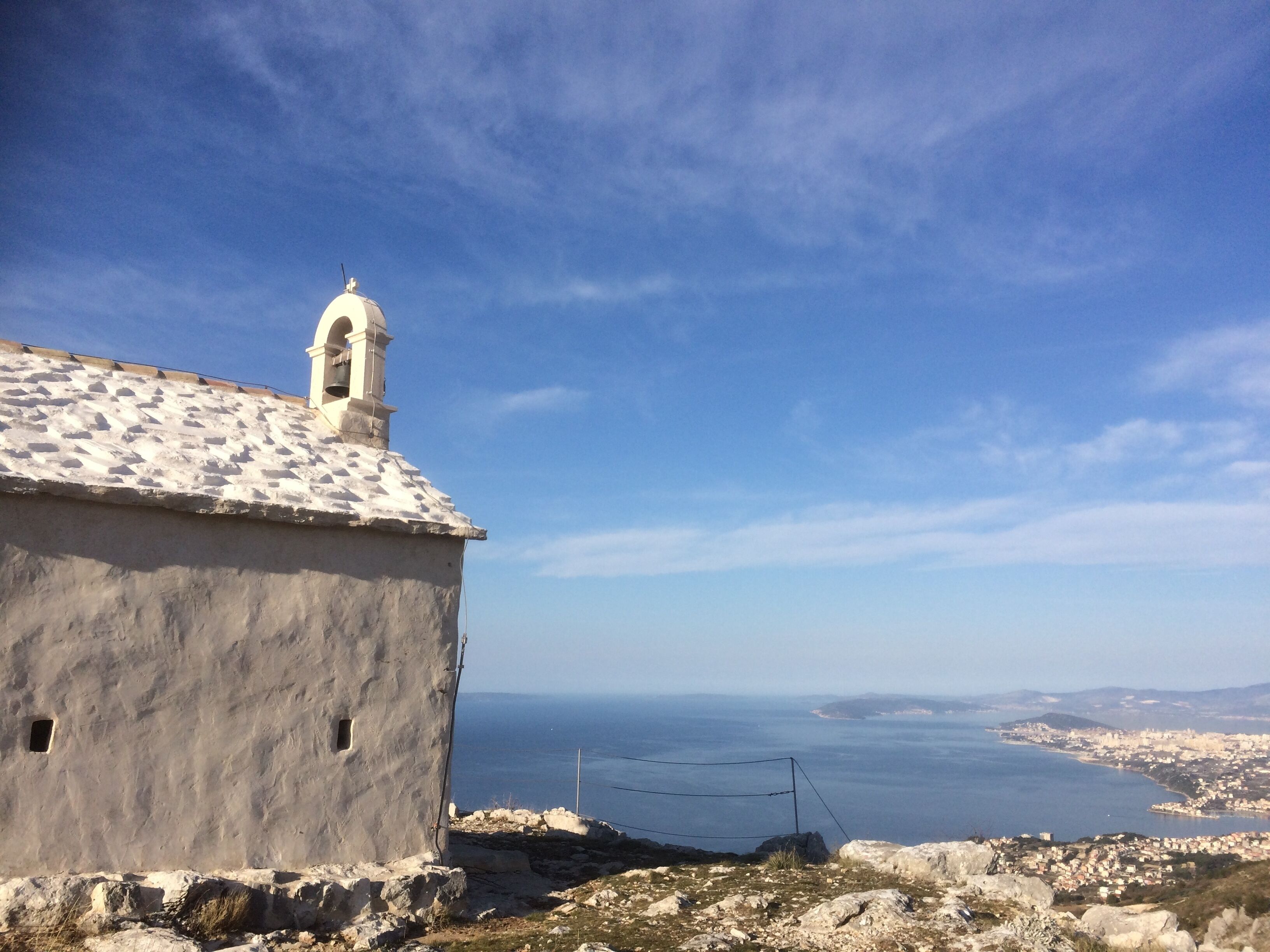 Un bâtiment blanc surmonté d’un clocher, qui domine une ville côtière et la mer.