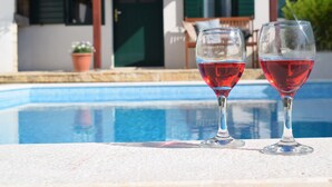 Dos copas de vino sobre una mesa junto a la piscina, con una piscina y una casa al fondo.