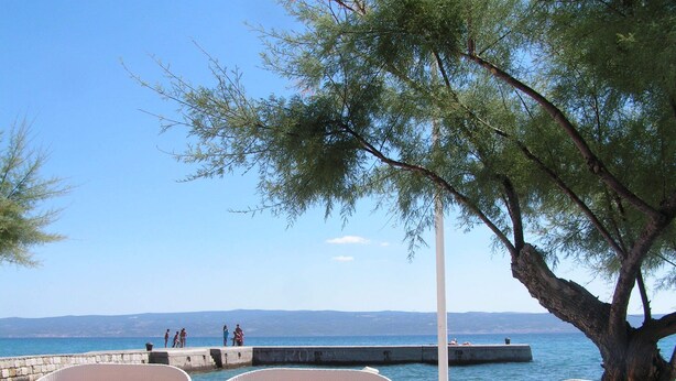 Una terraza frente al mar con sillones de mimbre y vistas al océano y colinas lejanas.