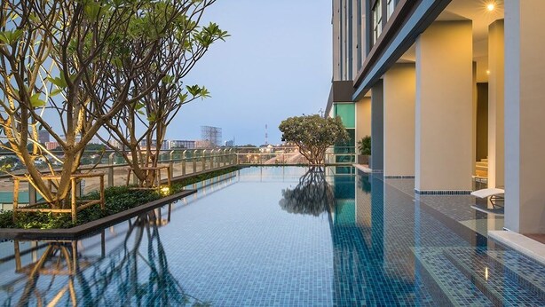 Un hôtel moderne doté d’une piscine à débordement sur le toit, entouré de verdure et offrant une vue sur la ville.