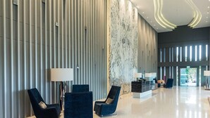 Un hall d’entrée moderne avec un mur de marbre, des stores verticaux et des fauteuils bleus.