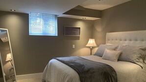 Un dormitorio con una cama grande, una mesita de noche con lámpara, una ventana con persianas y un cuadro en la pared.
