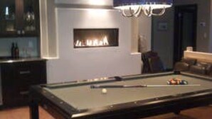 Una mesa de billar con una lámpara azul sobre ella, en una habitación con chimenea y zona de bar.