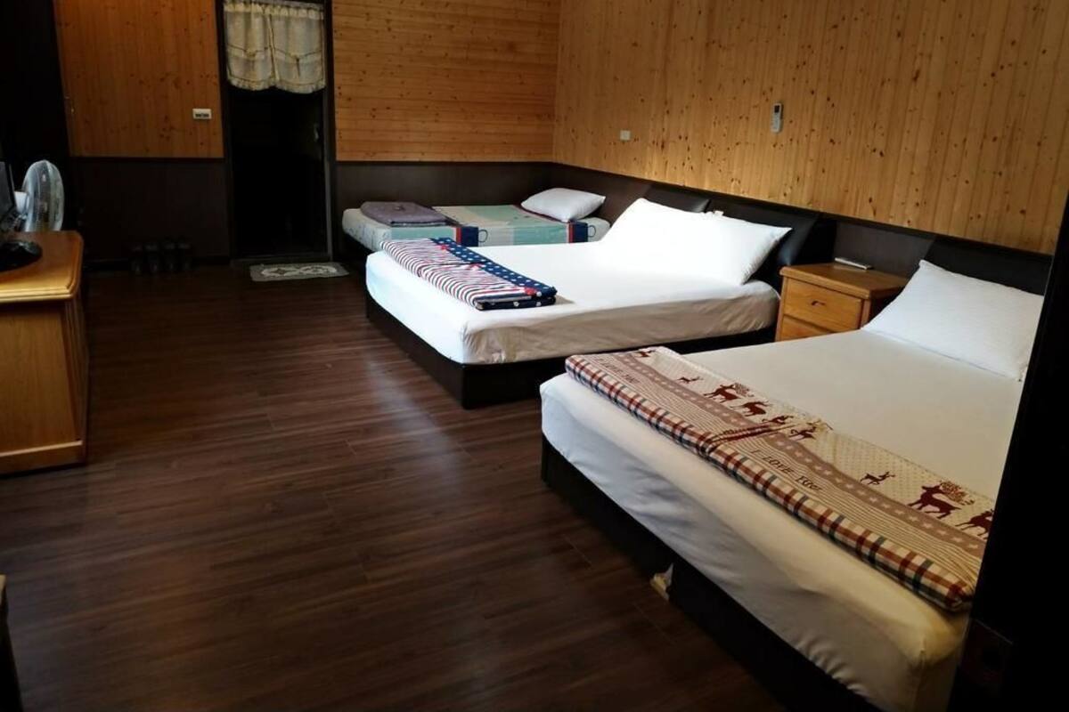 A hotel room with three beds, wooden flooring, and a wooden wall.