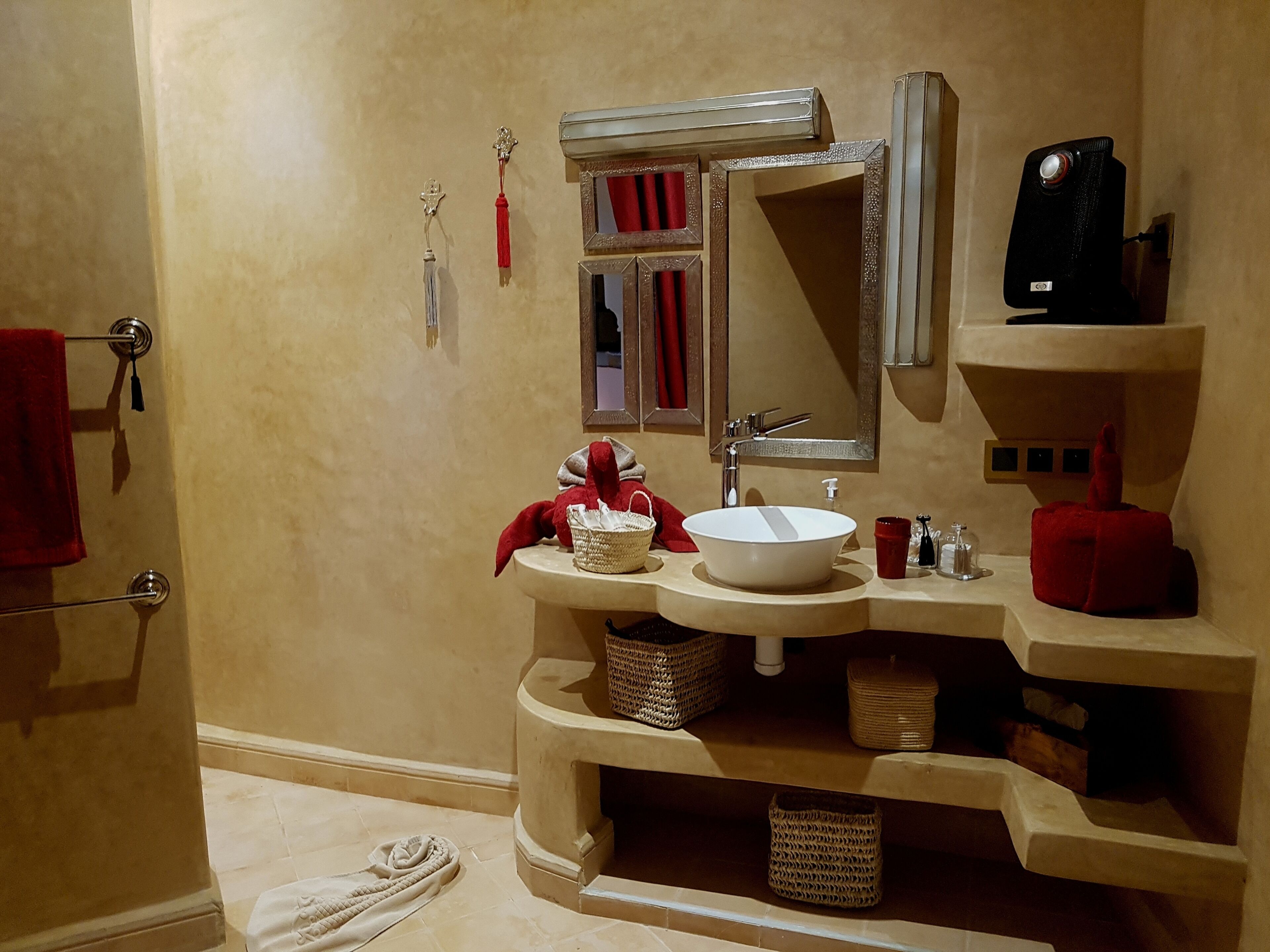 Een badkamer met een gebogen wastafel, een grote spiegel, een rode handdoek en een rode zeepdispenser.