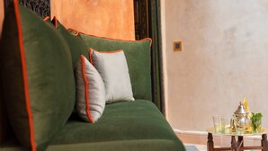 A green sofa with orange trim and a grey pillow, a small table with glasses and a silver pitcher, and a door with intricate metalwork. - Riad Bilkis Votre Maison à Marrakech (Marrakech)