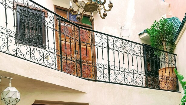 A courtyard with a wooden table and chairs, a colorful tiled floor, and a black door. - Riad Bilkis Votre Maison à Marrakech (Marrakech)