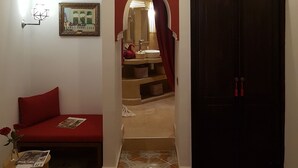A hallway with a red sofa, a framed picture, a wall-mounted air conditioner, and a dark wooden door. - Riad Bilkis Votre Maison à Marrakech (Marrakech)