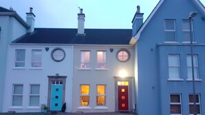 Una hilera de casas con puertas y ventanas diferentes, una calle en primer plano y un cielo despejado.