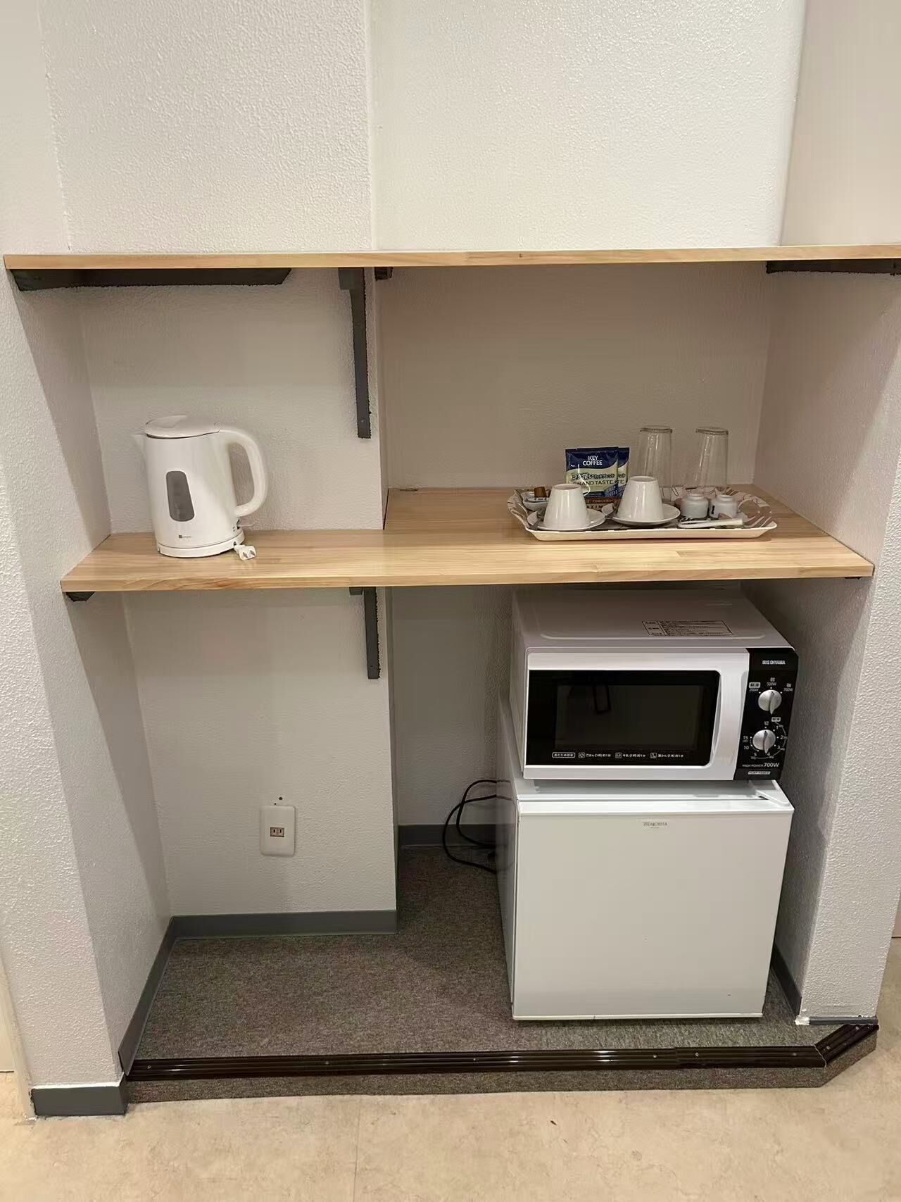 Una kitchenette compacta con microondas, hervidor y cafetera en un estante.