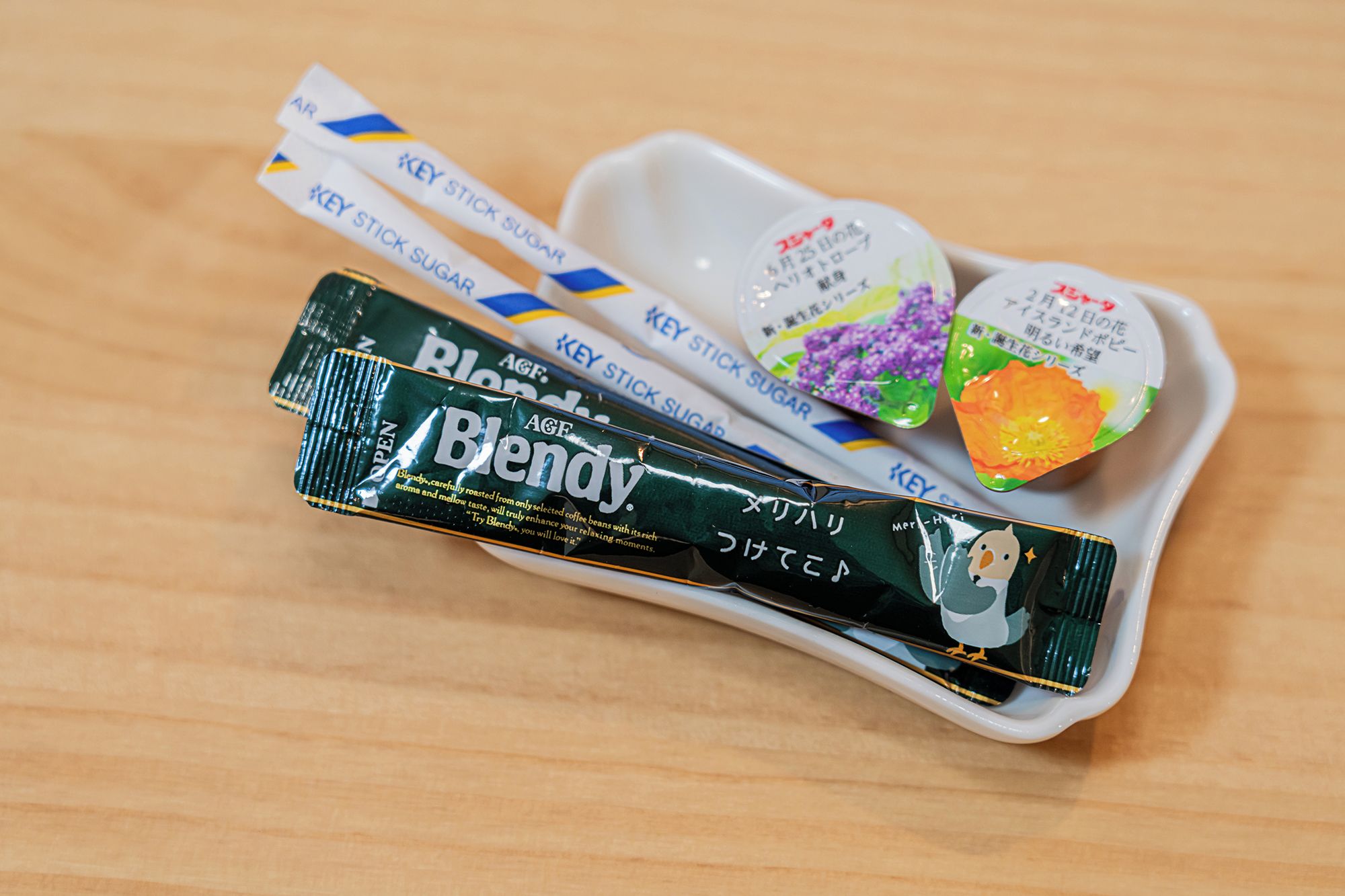 A tray with a package of A&G Blend coffee, a spoon with a sugar packet, and a small dish with colorful food items.