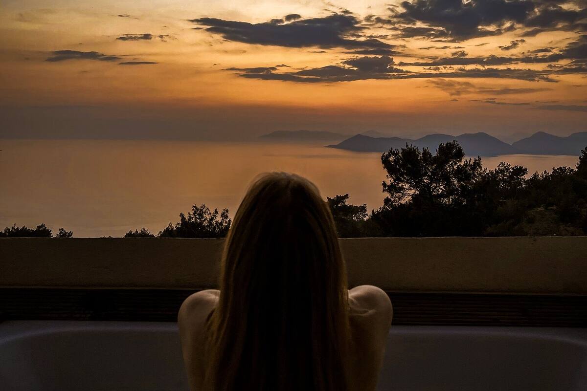 A person sitting in a bathtub overlooking a sunset view.