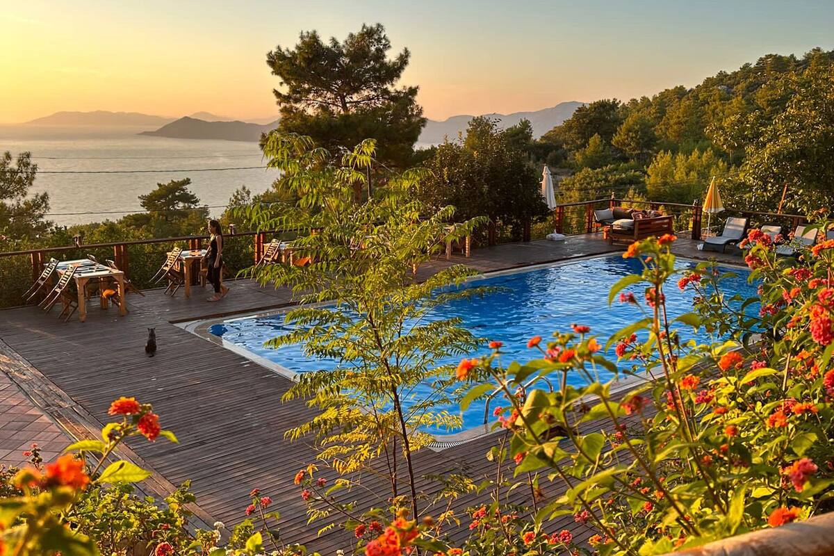 A poolside area with a wooden deck, lounge chairs, and a view of the sea and mountains.