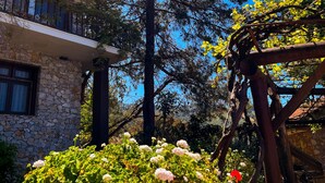 A stone building with a balcony, surrounded by lush greenery and a tall tree. - Faralia Hotel (Fethiye)