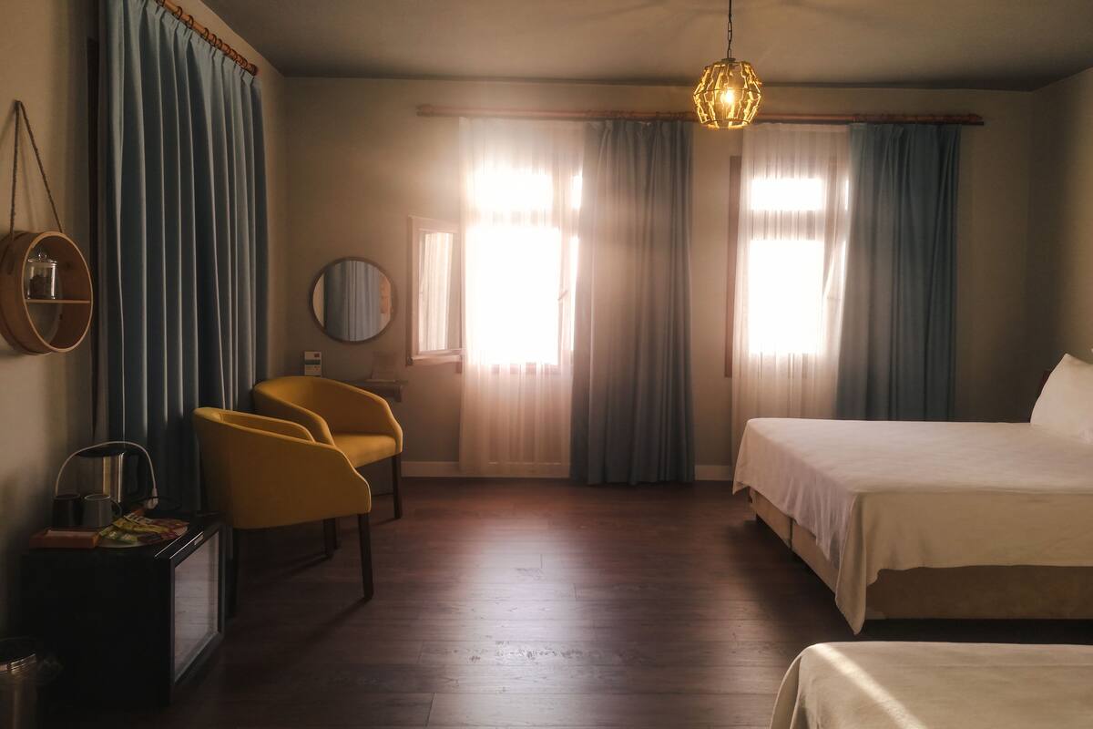 A hotel room with a bed, a chair, a small table, a mirror, and a hanging light fixture.