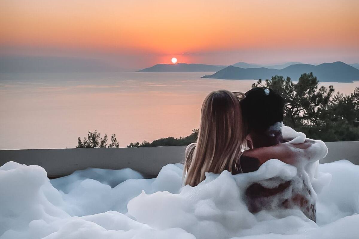 A couple embracing in a hot tub with a sunset view.