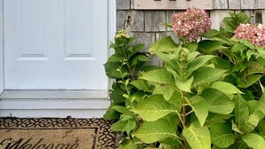 A white door with a window, a wooden mailbox, and a house number sign. - Cape Code Waterfront Cottage (Dennis Port)